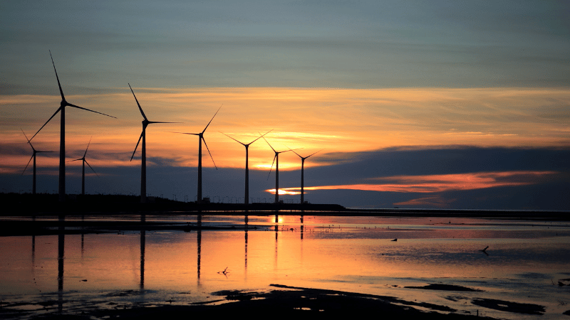 Sunset in the background with a silhouette of windmills symbolizing energy tax.