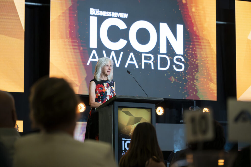 Lisa Donnelley speaking at a podium on stage in front of a large digital screen displaying the Idaho Business Review ICON Awards logo.