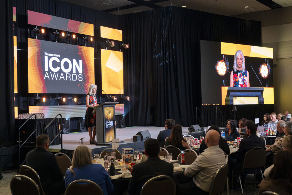 Wide view of an award ballroom banquet with Lisa Donnelley delivering an acceptance speech at the podium during the Idaho Business Review ICON Awards.