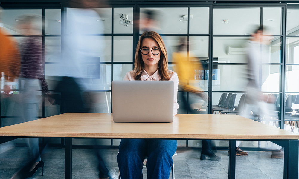 Business owner staying calm and focused at her desk amidst a fast-paced, hectic office environment.
